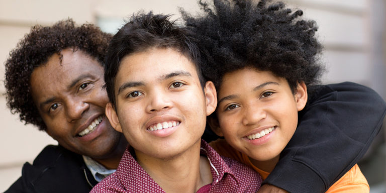 Portrait of an African American father hugging his sons.