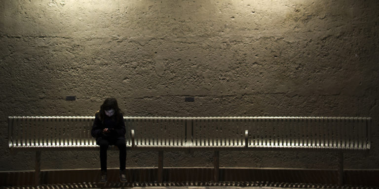 A young child sits alone on a bench with a mobile phone.
