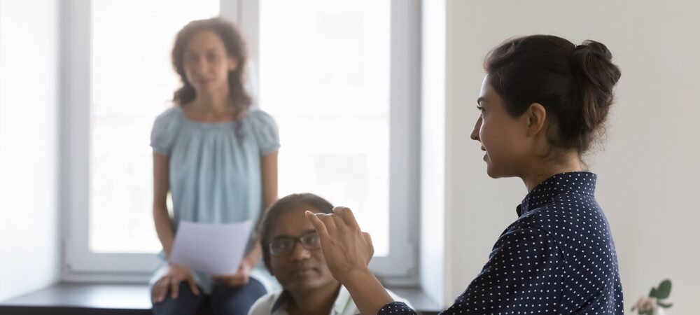Three diverse women, with two looking towards a third woman speaking.