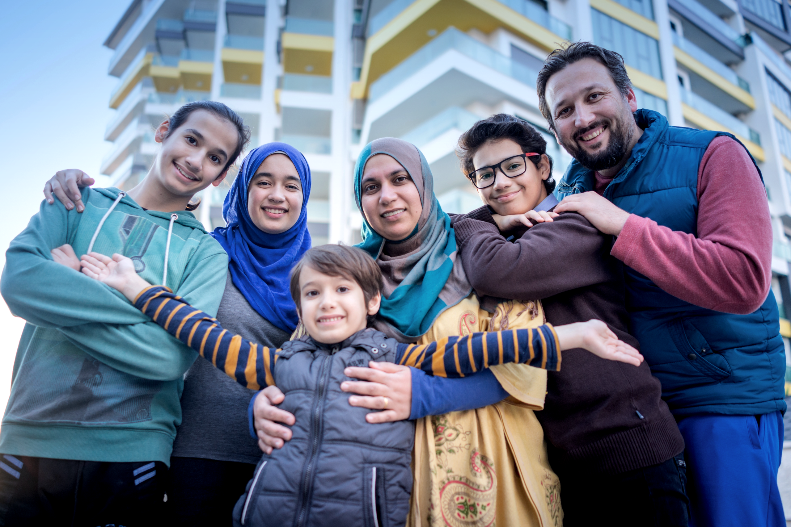A diverse family with two parents and four children smiling in front of a building.