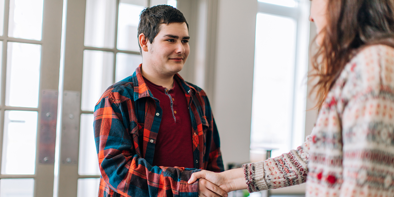 A man in a plaid shirt shaking hands with a woman to represent partnership and collaboration.