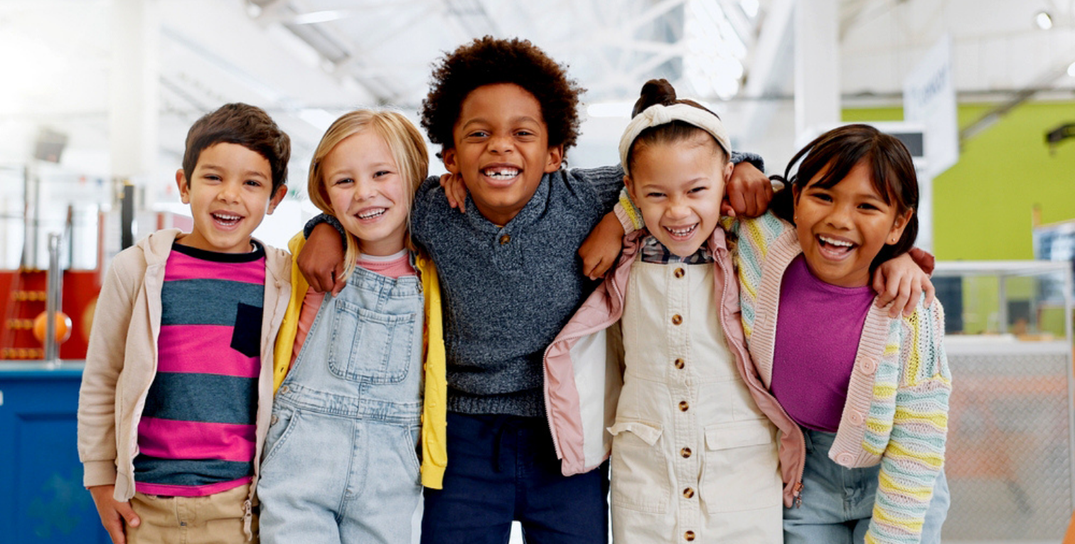 A diverse group of smiling children standing together with their arms around each other's shoulders.
