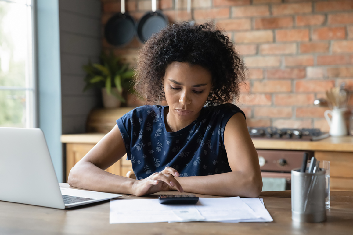 A woman working at a table with a laptop, calculator, and paperwork.