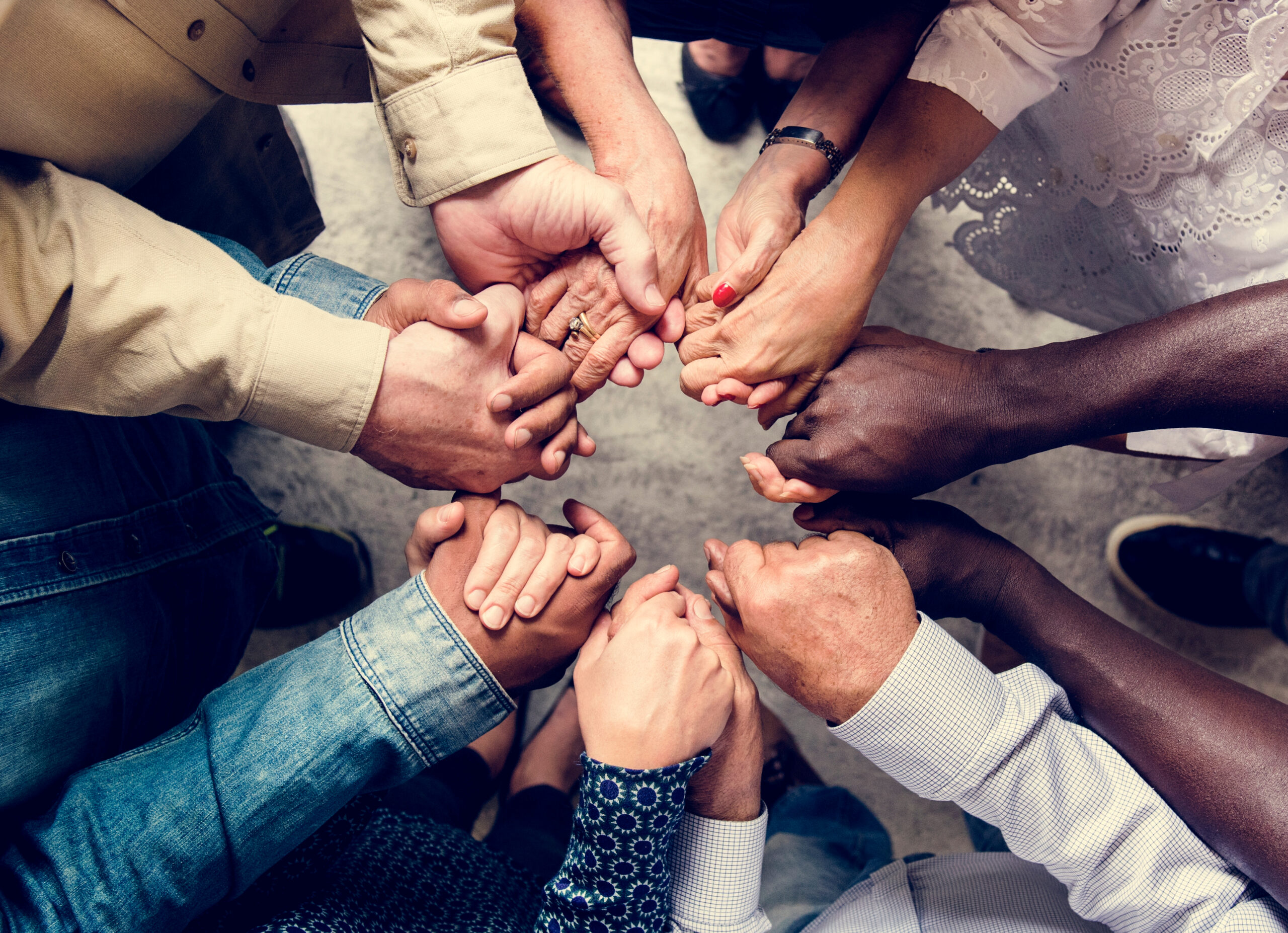 Diverse hands of different ages holding each other in a circle to represent unity and community.