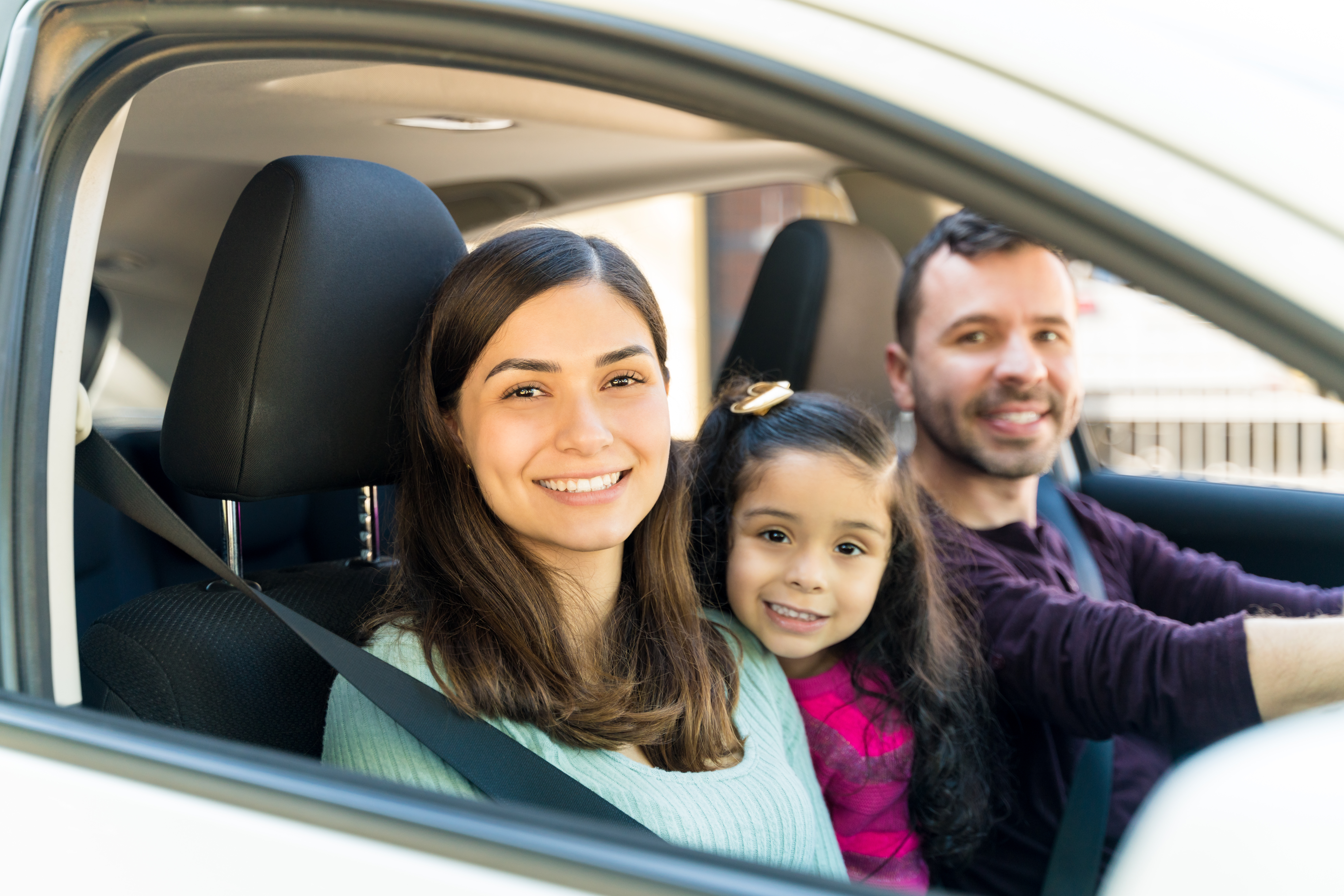 A smiling family in a car looking through the passenger window.