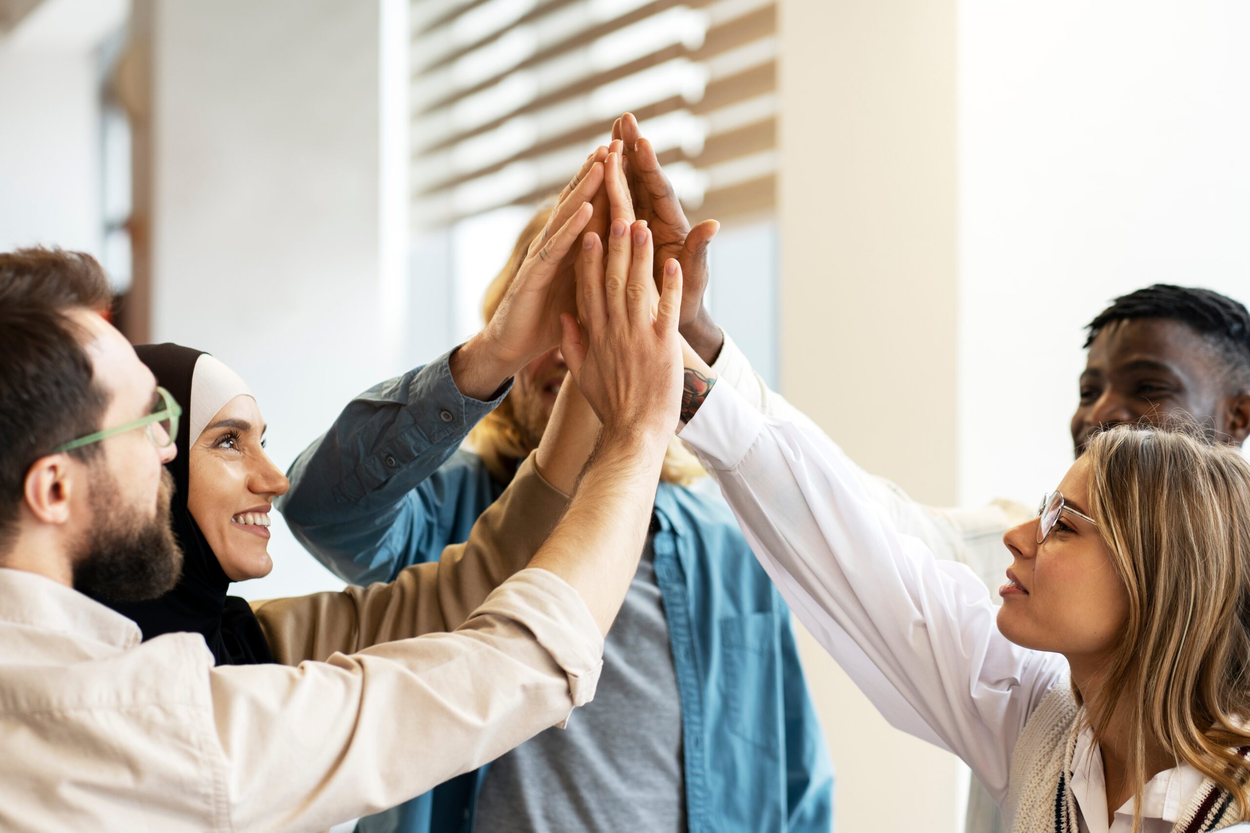 A diverse group of people smiling and raising their hands for a group high-five.