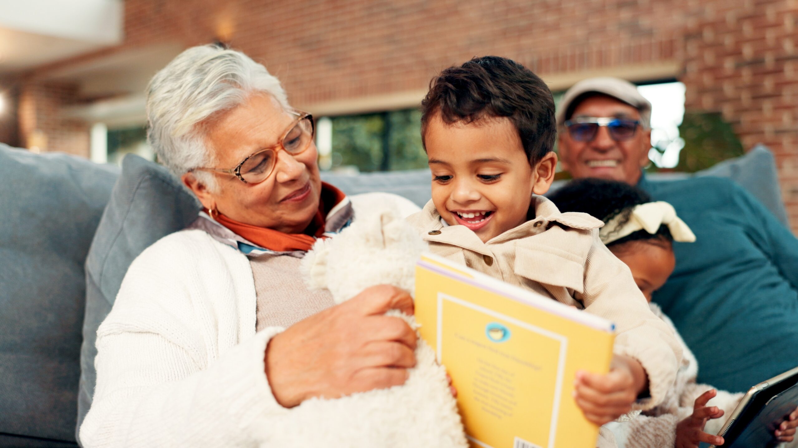 A older couple sitting on a couch with their grandchildren, smiling while holding a book.