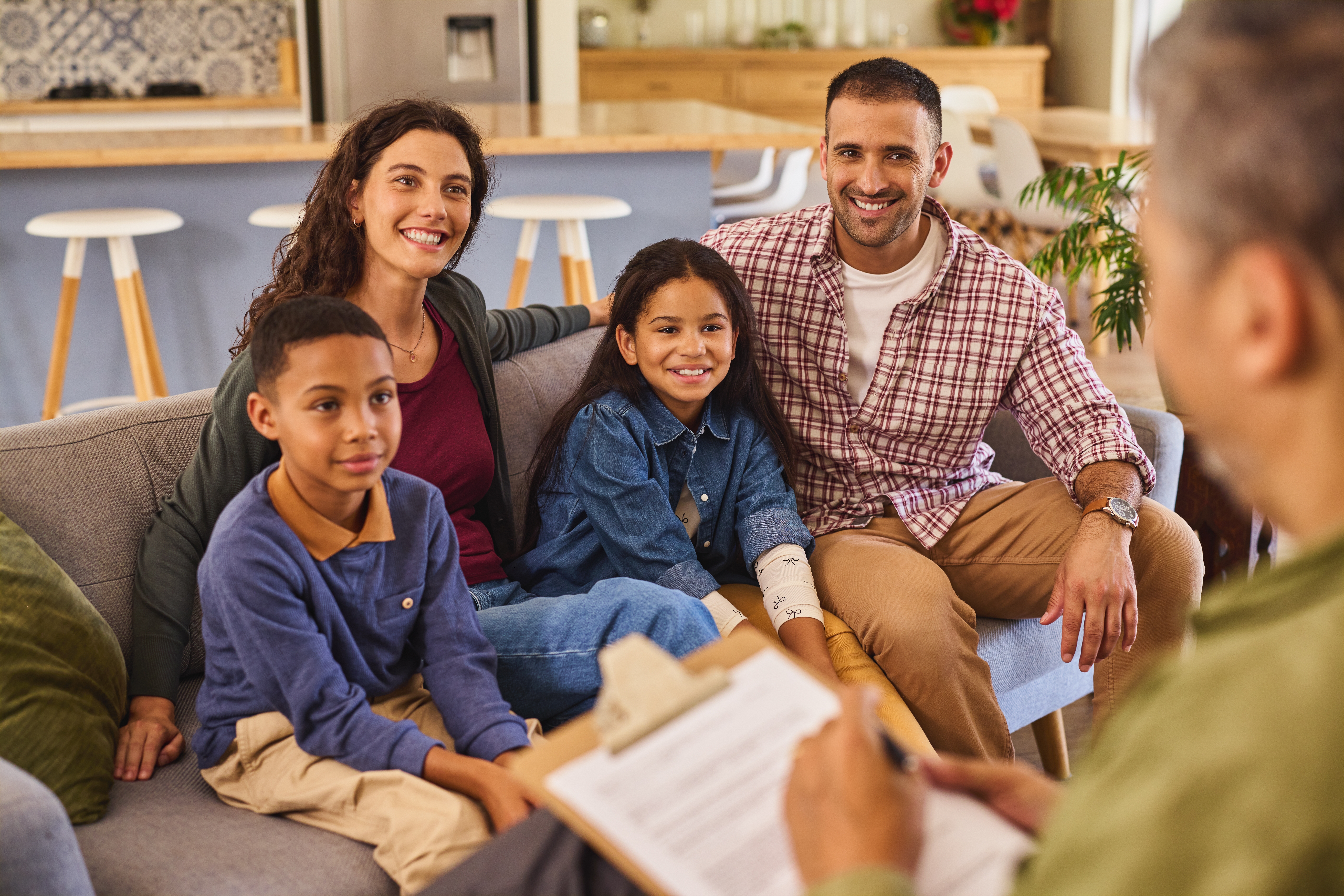 A diverse family with two children smiling together while sitting on a couch.